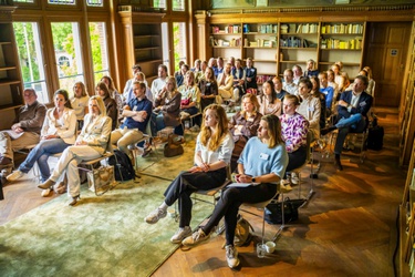 Een groep mensen in de Rijkszaal te luistert naar een presentatie