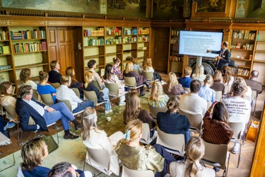 Een groep mensen in de Rijkszaal te luistert naar een presentatie